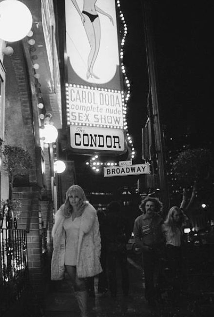 American striptease artist Carol Doda poses in a coat, miniskirt, and boots under a marquee baring her name outside the Condor, a strip bar in San Francisco, California, 1970s. (Photo by Tim Boxer/Getty Images)